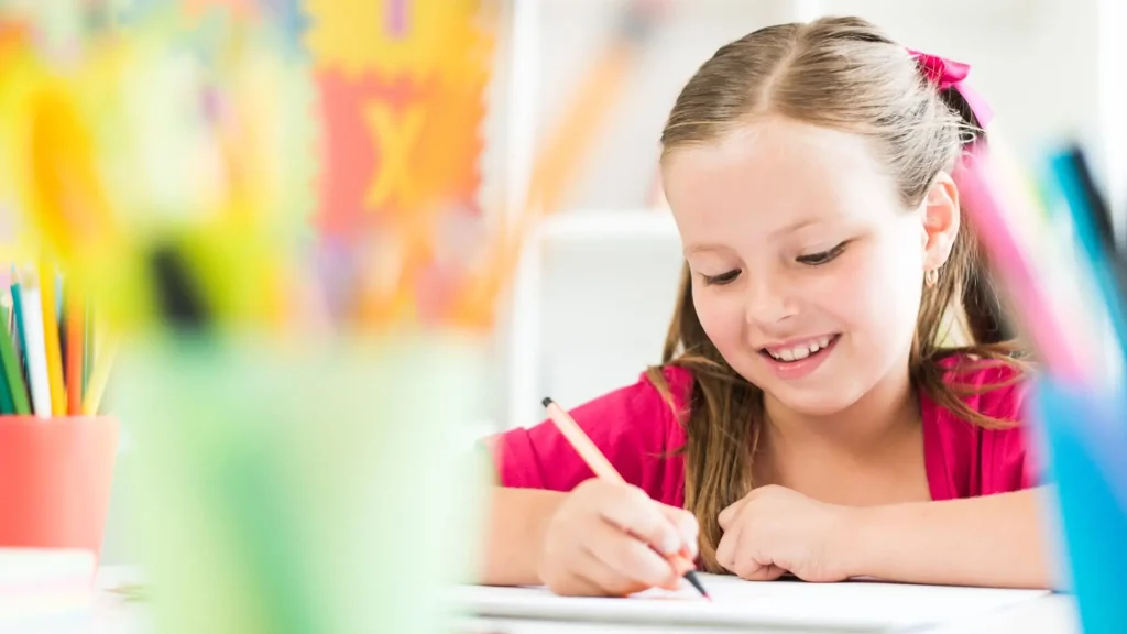 bambina sorridente che fa i compiti in autonomia, usando colori e matite